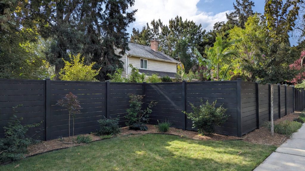 A sleek, modern black vinyl privacy fence surrounding a beautifully landscaped suburban yar