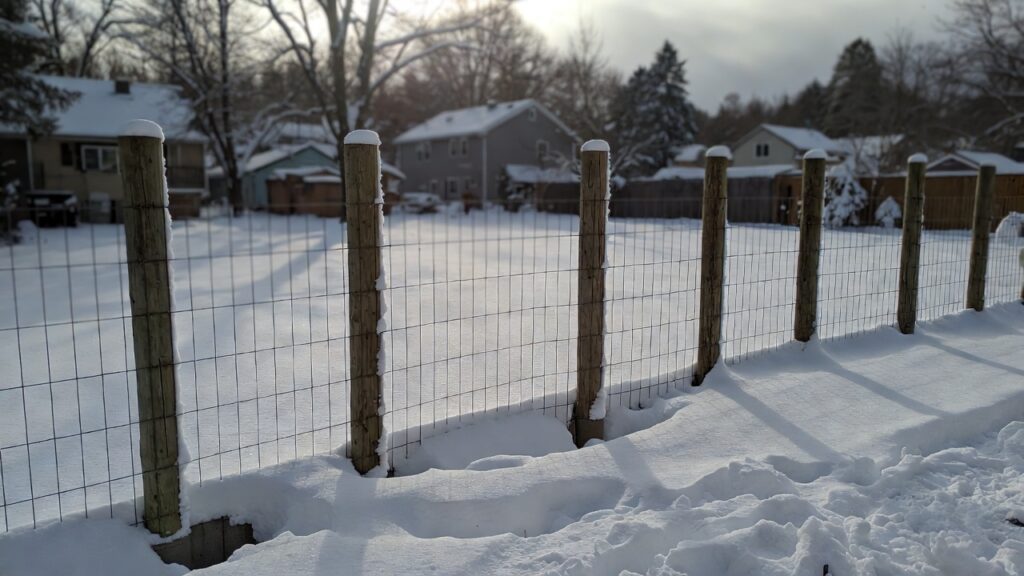 A newly installed frost fence with deep concrete footings in a snowy backyard. A newly installed frost fence with deep concrete footings in a snowy backyard.