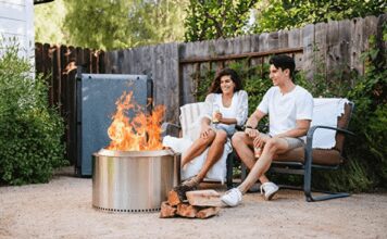 Solo Stove Reviews 2026: Bonfire vs. Yukon vs. Ranger A happy couple sitting on a backyard wood deck at dusk, relaxing in front of a burning, smokeless Solo Stove Bonfire fire pit.