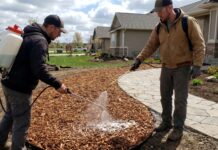 Mulch Glue: Does It Work, How Long It Lasts and When to Use It A landscaper spraying mulch glue on fresh wood chips to prevent washout and blowaway in a residential yard