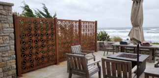 Best Privacy Screens for Windy Areas (2026): Wind-Resistant Options That Actually Work A heavy-duty metal privacy screen securely anchored on a windy patio with patio furniture.