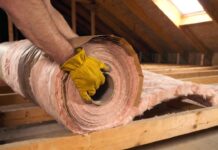 Faced vs Unfaced Insulation: The Ultimate Guide for Your Home A DIY homeowner installing faced fiberglass insulation with a kraft paper vapor barrier between wooden attic joists.