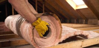 Faced vs Unfaced Insulation: The Ultimate Guide for Your Home A DIY homeowner installing faced fiberglass insulation with a kraft paper vapor barrier between wooden attic joists.