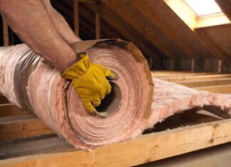 Faced vs Unfaced Insulation: The Ultimate Guide for Your Home A DIY homeowner installing faced fiberglass insulation with a kraft paper vapor barrier between wooden attic joists.