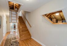 Best Attic Doors: Access Panels, Pull-Down Stairs & Insulated Options A white attic access door in a hallway ceiling with pull-down attic stairs partially opened