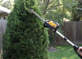 DEWALT Pole Hedge Trimmer Review: Is DCPH820 Worth Itdewalt-pole-hedge-trimmer? DEWALT cordless pole hedge trimmer cutting the top of a tall backyard privacy hedge from ground level