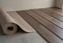 Underlayment for Engineered Hardwood Flooring: What Goes Under It? Roll of underlayment beneath engineered hardwood flooring planks on a prepared subfloor