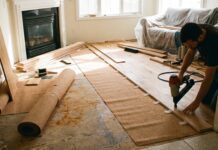 Tongue and Groove Flooring: Costs, Pros, Cons & Install Tips Tongue and groove wood flooring planks being installed with a flooring nailer, spacers, and underlayment in a living room renovation