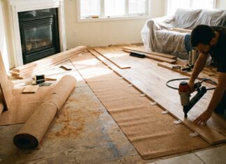 Tongue and Groove Flooring: Costs, Pros, Cons & Install Tips Tongue and groove wood flooring planks being installed with a flooring nailer, spacers, and underlayment in a living room renovation