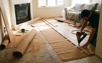 Tongue and Groove Flooring: Costs, Pros, Cons & Install Tips Tongue and groove wood flooring planks being installed with a flooring nailer, spacers, and underlayment in a living room renovation